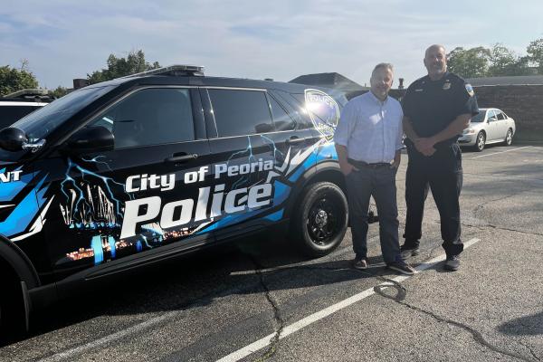 Congressman Eric Sorensen and local law enforcement officer stand next to police vehicle