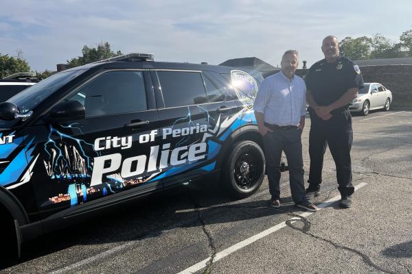 Congressman Eric Sorensen and police officer stand in front of department vehicle