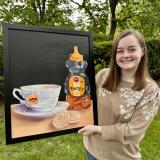 Student holds painting depicting tea, honey, and cookies;