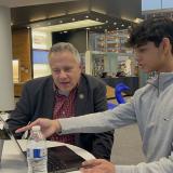 Congressman Eric Sorensen looks on as high school student points to a computer screen and explains a software application the student developed.